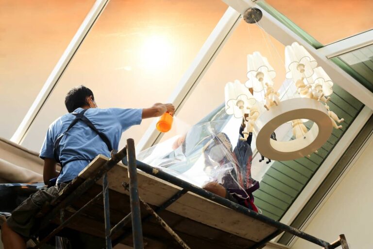 Unidentified people wrappers tinting a glass house window with tinted foil or film using foggy spray